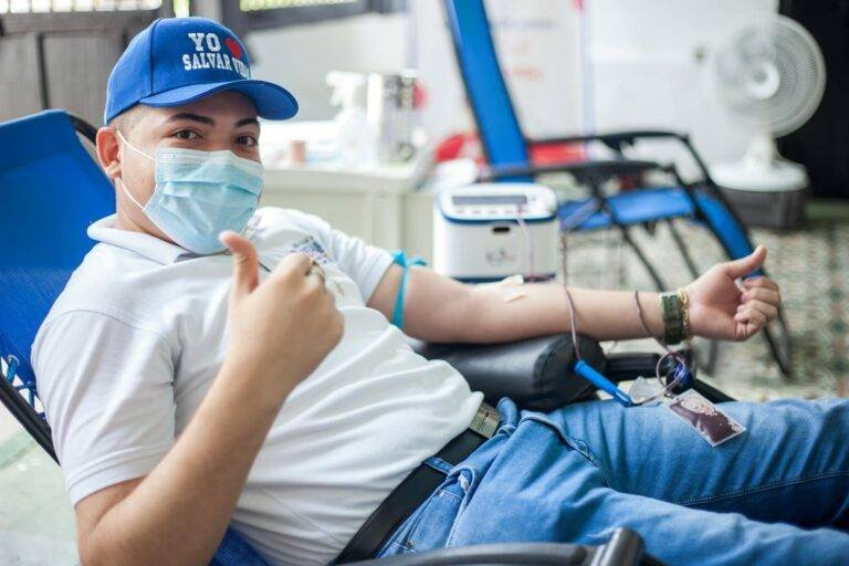a man in white polo shirt donating blood while looking at the camera