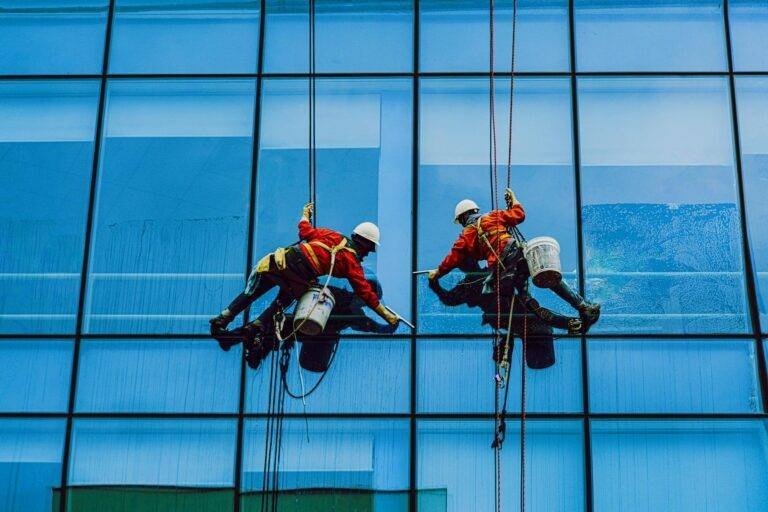 men hanging in ropes cleaning the building glass windows