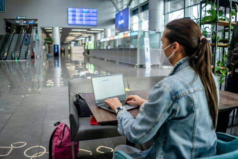 focused woman in mask browsing laptop in airport