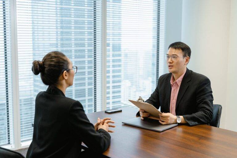 man in glasses holding a folder while talking to a woman in suit