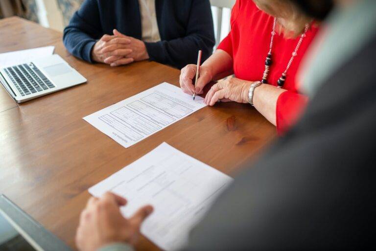 woman signing a contract in an office in the presence of lawyers