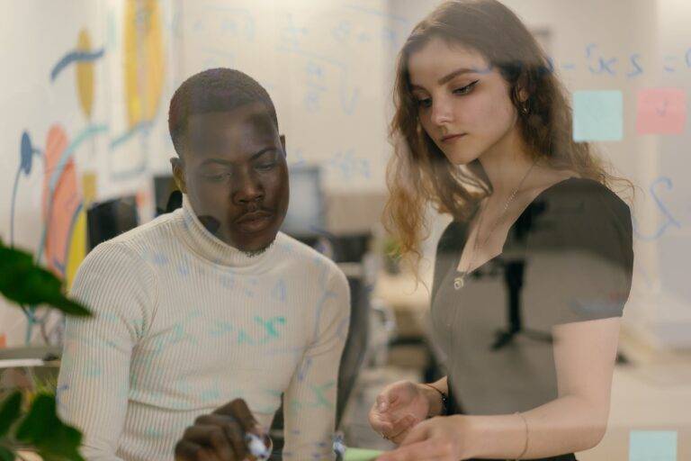 man and woman writing with pen on glass in office