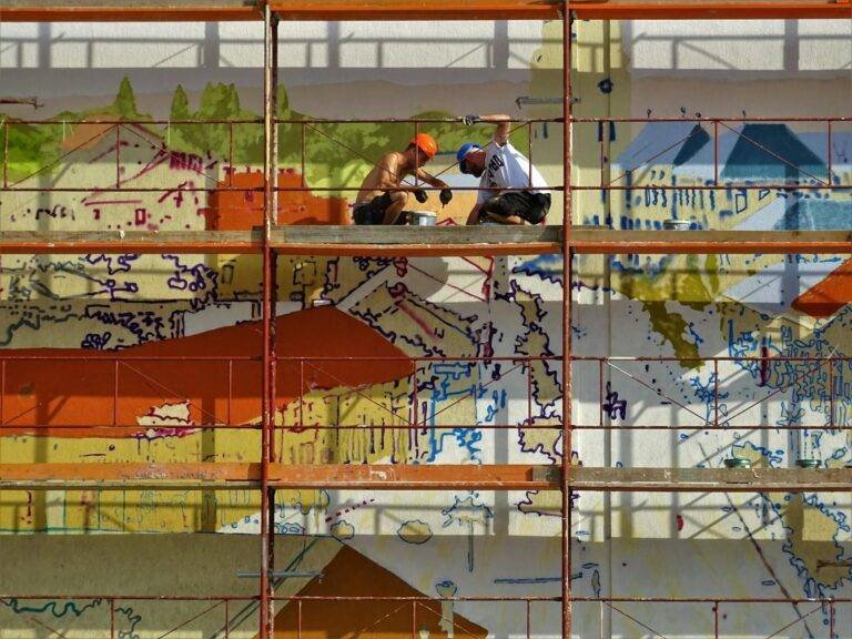 two person on scaffolding painting wall