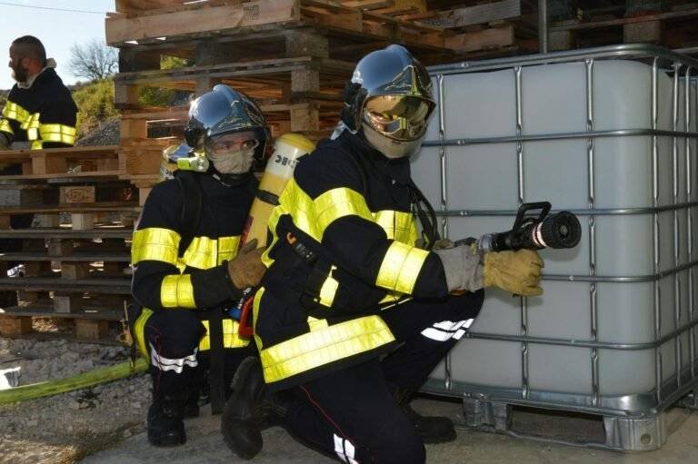 photo of firefighters with a fire hose crouching next to a water tank