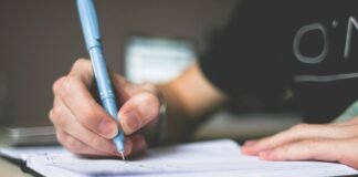person holding blue ballpoint pen writing in notebook