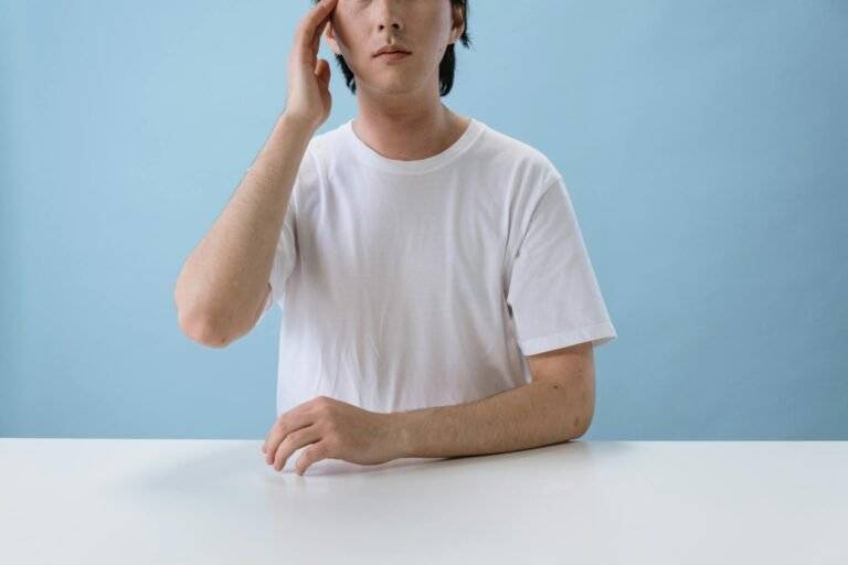 man in white t shirt sitting and touching head