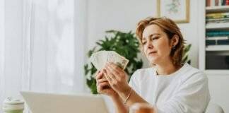 woman sitting in front of a laptop and holding a bunch of cash
