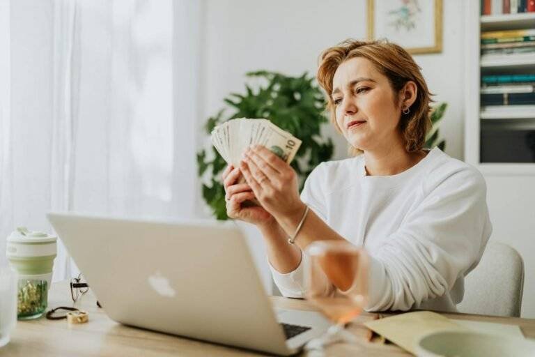 woman sitting in front of a laptop and holding a bunch of cash