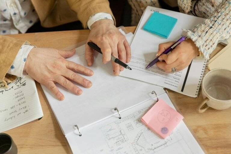 close up of people sitting at the desk reading and writing in documents