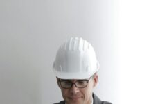 serious engineer working on laptop with blueprints