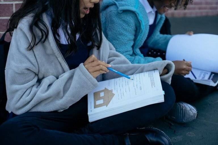 young diverse pupils studying lesson together while sitting in yard