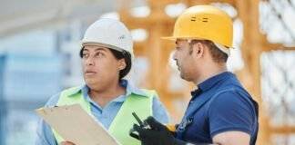 woman in blue long sleeve shirt wearing white hard hat holding white clipboard
