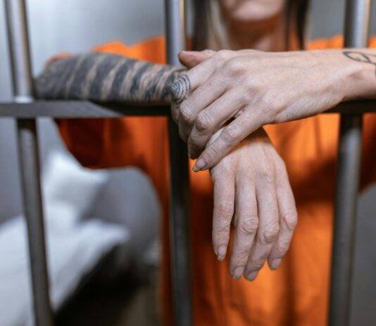 hands of a person with tattoo hanging from steel bars