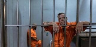 man in orange jacket leaning on gray metal bars