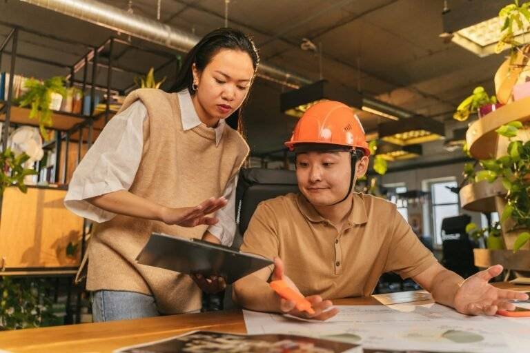 a woman standing near the man in orange hard hat while having conversation