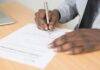 person holding gray twist pen and white printer paper on brown wooden table