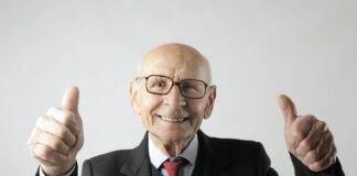 positive senior man in eyeglasses showing thumbs up and looking at camera
