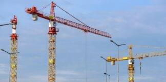 three yellow and red tower cranes under clear blue sky
