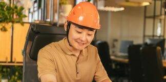 man in brown polo shirt and orange hard hat smiling while writing on paper
