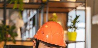 man in brown polo shirt wearing orange hard hat while writing