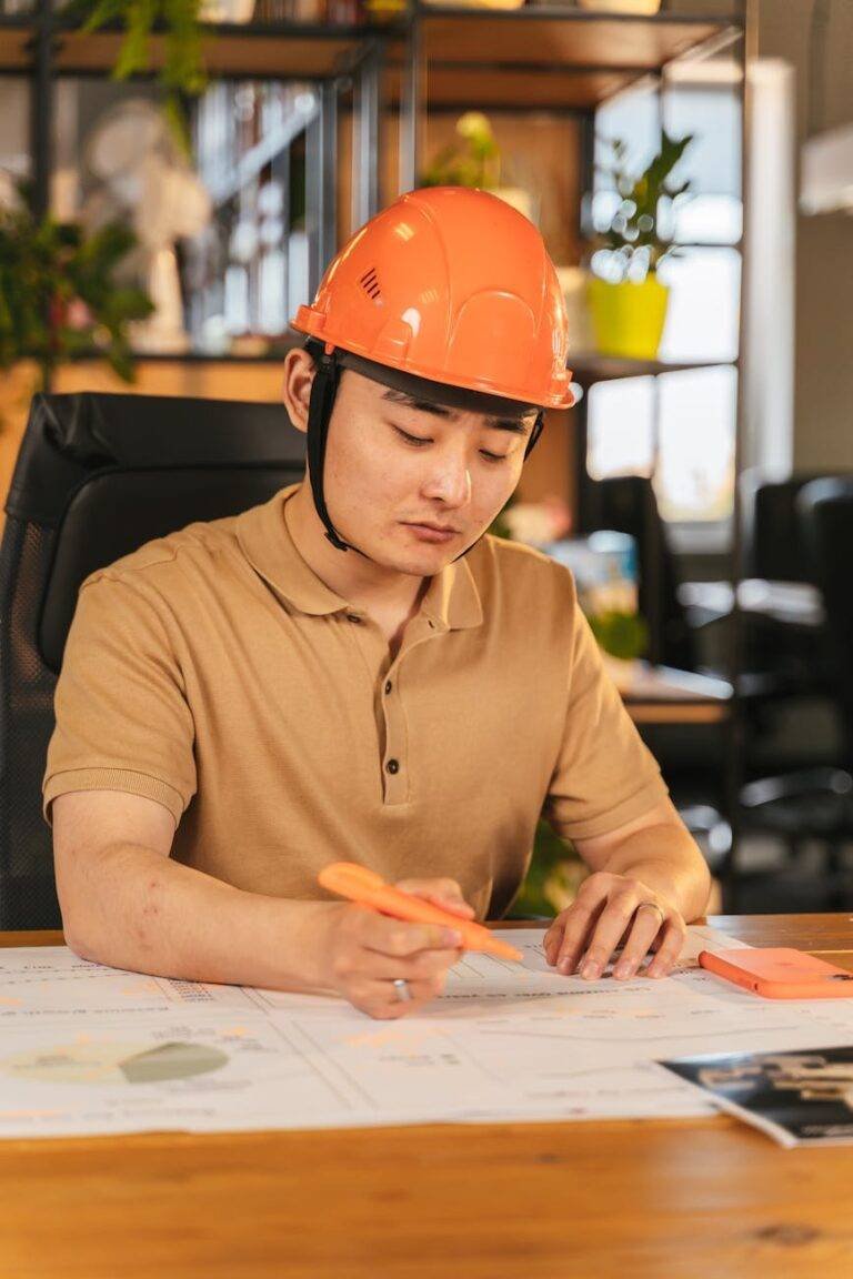 man in brown polo shirt wearing orange hard hat while writing
